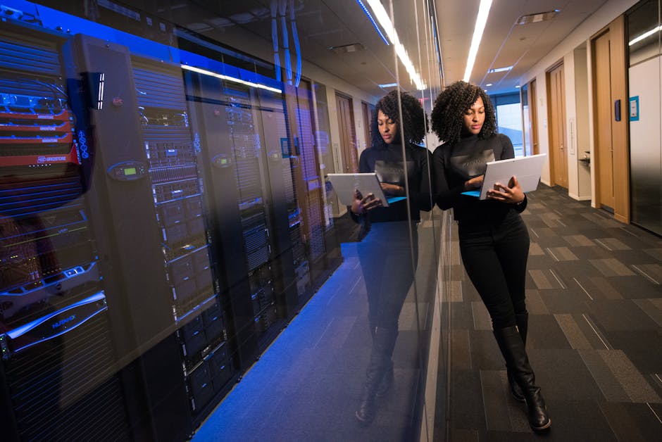 pexels-photo-1181316-1181316 A woman using a laptop navigating a contemporary data center with mirrored servers.